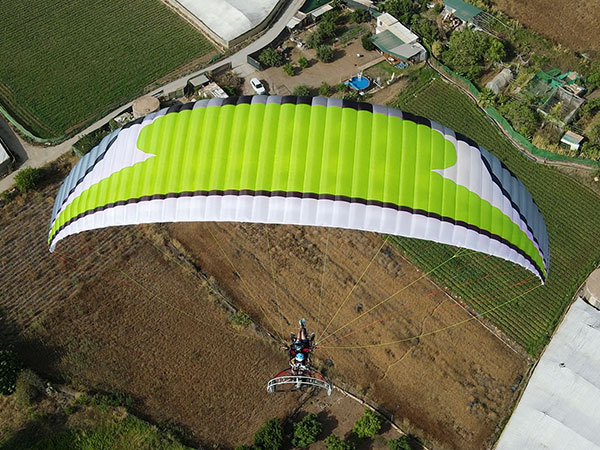 Windtech Mad Max 2 paramotor wing in lime green — aerial shot of pilot in flight over farmland