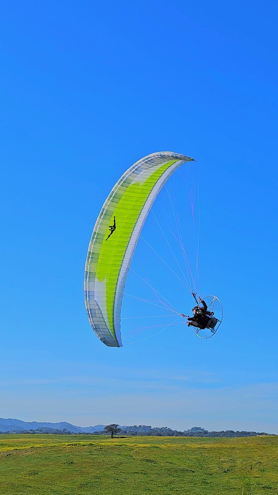 Pilot flying an HE paramotor under a lime Windtech wing